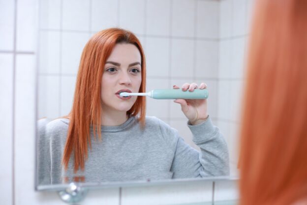 SLS ist die Abkürzung für Sodium Lauryl Sulfate, auf Deutsch Natriumlaurylsulfat. Der Stoff gehört zu den Tensiden und sorgt dafür, dass sich Zahnpasta beim Putzen schnell im Mund verteilt und kräftig aufschäumt. Tenside verringern die Oberflächenspannung und helfen dabei, Speisereste, Fette und gelöste Ablagerungen mit dem Speichel zu vermischen. Das üppige Schaumgefühl vermittelt vielen Menschen den Eindruck einer besonders gründlichen Reinigung. Für den eigentlichen Kariesschutz ist SLS jedoch nicht verantwortlich. Der Stoff unterstützt in erster Linie die Verteilung und das gewohnte Mundgefühl einer Zahnpasta, während andere Bestandteile für Abrieb, Remineralisierung, Geschmack und Schutzwirkung zuständig sind. Eine Zahnpasta kann deshalb auch ohne SLS gründlich reinigen und einen wirksamen Kariesschutz bieten. Viel Schaum bedeutet nicht automatisch saubere Zähne Die Schaummenge einer Zahncreme sagt wenig darüber aus, wie gründlich sie die Zähne tatsächlich reinigt. Entscheidend sind vor allem die Bewegung der Zahnbürste, die erreichten Zahnflächen, die Putzdauer und die in der Zahnpasta enthaltenen Putzkörper und Wirkstoffe. SLS-freie Zahncremes schäumen häufig nur schwach oder beinahe gar nicht. Das kann während der ersten Anwendungen ungewohnt wirken, weil das vertraute Frische- und Sauberkeitsgefühl fehlt. Die Zähne werden dadurch aber nicht zwangsläufig schlechter gereinigt. Im Gegenteil: Weniger Schaum erleichtert manchen Menschen sogar den Überblick, weil sie die Bürste und die einzelnen Zahnflächen im Spiegel besser erkennen können. Zusätzliche Zahnpasta auf die Bürste zu geben, verbessert die Reinigung nicht, sondern erhöht lediglich den Verbrauch. Was SLS mit empfindlicher Mundschleimhaut machen kann Die Mundschleimhaut bildet eine empfindliche Schutzbarriere, die täglich mit Lebensmitteln, Getränken, Bakterien und Pflegeprodukten in Kontakt kommt. Bei den meisten Menschen verursacht SLS in den üblichen Konzentrationen keine auffälligen Beschwerden. Empfindliche Personen können nach dem Putzen jedoch ein Brennen, Spannungsgefühl, eine trockene Schleimhaut oder ein oberflächliches Ablösen kleiner Schleimhautbereiche beobachten. Wissenschaftliche Übersichtsarbeiten beschreiben mögliche Zusammenhänge zwischen SLS-haltigen Zahnpasten und Schleimhautreizungen, Entzündungsreaktionen oder einer verstärkten Abschilferung oberflächlicher Zellen. Das bedeutet nicht, dass SLS grundsätzlich schädlich ist. Es zeigt vielmehr, dass ein verbreiteter Inhaltsstoff nicht von jedem Mund gleich gut vertragen wird. Aphthen sind mehr als eine kleine Verletzung im Mund Aphthen sind rundliche oder ovale, meist weißlich belegte und von einem roten Rand umgebene Schleimhautstellen. Sie treten häufig an den Innenseiten der Lippen und Wangen, unter der Zunge oder am weichen Gaumen auf. Obwohl sie klein sein können, verursachen sie beim Essen, Trinken, Sprechen und Zähneputzen teilweise erhebliche Schmerzen. Einzelne Aphthen verschwinden normalerweise von selbst, doch manche Menschen entwickeln immer wieder neue Stellen. In diesem Fall spricht man von wiederkehrenden oder rezidivierenden Aphthen. Ihre Entstehung lässt sich häufig nicht auf eine einzelne Ursache reduzieren. Kleine Verletzungen, Stress, bestimmte Lebensmittel, hormonelle Einflüsse, Mangelzustände und Erkrankungen können eine Rolle spielen. Auch reizende Zahnpastabestandteile werden als mögliche Verstärker diskutiert. Der Zusammenhang zwischen SLS und Aphthen ist plausibel, aber nicht eindeutig Mehrere klinische Untersuchungen haben geprüft, ob Menschen mit wiederkehrenden Aphthen von einer Zahnpasta ohne SLS profitieren. Eine systematische Übersichtsarbeit kam zu dem Ergebnis, dass SLS-freie Zahncremes die Anzahl der Geschwüre, ihre Dauer, die Häufigkeit der Episoden und die wahrgenommenen Schmerzen verringern könnten. Die ausgewerteten Studien waren allerdings klein und unterschieden sich teilweise in ihrem Aufbau. Einzelne Untersuchungen fanden vor allem eine schnellere Heilung und weniger Schmerzen, ohne eine deutliche Verringerung der Zahl neuer Aphthen festzustellen. Die wissenschaftlich angemessene Aussage lautet deshalb nicht, dass SLS Aphthen verursacht, sondern dass ein Verzicht bei wiederkehrenden Beschwerden einen sinnvollen Versuch darstellen kann. Eine SLS-freie Zahnpasta ist keine Behandlung für jede Aphthe Der Wechsel der Zahncreme beseitigt weder mögliche Grunderkrankungen noch mechanische Ursachen. Eine scharfe Zahnkante, eine schlecht sitzende Prothese, eine feste Zahnspange oder wiederholtes Beißen auf dieselbe Stelle können die Schleimhaut unabhängig von der Zahnpasta verletzen. Ebenso wenig behebt eine neue Zahncreme einen Eisen-, Vitamin-B12- oder Folsäuremangel. SLS-freie Zahnpasta sollte daher als schonende Anpassung der täglichen Mundpflege verstanden werden, nicht als universelle Therapie. Zeigen sich nach dem Wechsel weniger Beschwerden, spricht das für eine individuelle Unverträglichkeit oder Reizempfindlichkeit. Bleibt alles unverändert, sollte die Suche nach anderen Auslösern nicht durch einen immer häufigeren Produktwechsel ersetzt werden. Für wen sich der Wechsel besonders anbieten kann Ein Versuch mit SLS-freier Zahnpasta ist vor allem für Menschen interessant, die regelmäßig unter Aphthen leiden oder nach dem Zähneputzen wiederholt Brennen und gereizte Schleimhäute bemerken. Auch bei ausgeprägter Mundtrockenheit kann eine mild formulierte Zahncreme angenehmer sein, weil trockene Schleimhaut weniger widerstandsfähig gegenüber mechanischen und chemischen Reizen ist. Dasselbe gilt während bestimmter zahnärztlicher oder kieferorthopädischer Behandlungen, wenn die Mundschleimhaut ohnehin beansprucht wird. Wer dagegen keinerlei Beschwerden verspürt und mit seiner bisherigen Zahnpasta zufrieden ist, muss SLS nicht vorsorglich meiden. Die Verträglichkeit eines Pflegeprodukts ist eine individuelle Frage und kein Wettbewerb um die kürzeste Inhaltsstoffliste. So lässt sich SLS auf der Verpackung erkennen Auf der Liste der Inhaltsstoffe erscheint SLS üblicherweise unter der englischen Bezeichnung „Sodium Lauryl Sulfate“. Vereinzelt finden sich auch Bezeichnungen wie Natriumlaurylsulfat oder Sodium Dodecyl Sulfate. Der ähnlich klingende Stoff Sodium Laureth Sulfate, kurz SLES, ist chemisch nicht identisch, gehört aber ebenfalls zu den schäumenden Tensiden. Wer eine möglichst milde Zahncreme sucht, sollte deshalb nicht nur nach einem großen Hinweis wie „SLS-frei“ Ausschau halten, sondern die vollständige Deklaration prüfen. Manche Hersteller verwenden anstelle von SLS mildere Tenside, andere verzichten weitgehend auf Schaumbildner. „SLS-frei“ bedeutet daher nicht automatisch „tensidfrei“, „allergenfrei“ oder für jeden Menschen gleichermaßen gut verträglich. Fluoridfrei und SLS-frei sind zwei unterschiedliche Eigenschaften Beim Einkauf werden SLS-freie Zahnpasten häufig mit Naturkosmetik oder fluoridfreien Produkten verwechselt. Beide Entscheidungen haben jedoch nichts miteinander zu tun. Eine Zahncreme kann ohne SLS auskommen und trotzdem Fluorid enthalten. Für die meisten Erwachsenen ist genau diese Kombination besonders interessant: eine milde Rezeptur ohne den möglicherweise reizenden Schaumbildner, aber mit bewährtem Kariesschutz. Die aktuelle deutsche S3-Leitlinie empfiehlt ab dem Durchbruch der bleibenden Zähne Zahnpasta mit mindestens 1.000 ppm Fluorid. Handelsübliche Erwachsenenzahnpasten enthalten meistens zwischen 1.000 und 1.500 ppm. Wer lediglich SLS meiden möchte, sollte deshalb nicht unbeabsichtigt auch auf Fluorid verzichten. Eine milde Zahnpasta darf trotzdem wirksam sein Sanfte Zahncreme wird häufig mit geringer Reinigungsleistung gleichgesetzt. Dabei können auch SLS-freie Produkte Fluorid, geeignete Putzkörper und Wirkstoffe gegen empfindliche Zähne enthalten. Wichtiger als ein intensiver Geschmack ist, ob die Zusammensetzung zum persönlichen Bedarf passt. Menschen mit empfindlichen Zahnhälsen sollten zusätzlich auf einen niedrigen oder moderaten Abrieb achten. Wer stark zu Karies neigt, benötigt einen ausreichenden Fluoridgehalt. Bei Mundtrockenheit sind milde Aromen und eine wenig reizende Rezeptur meist angenehmer als intensive Minze oder besonders stark schäumende Zahncremes. Die Aufschrift „ohne SLS“ beantwortet somit nur eine von mehreren Fragen, die bei der Auswahl berücksichtigt werden sollten. Der fehlende Schaum verändert zunächst die Putzroutine Viele Nutzer sind beim ersten Putzen mit einer SLS-freien Zahnpasta enttäuscht, weil sich kaum Schaum entwickelt und der Mund weniger intensiv nach Minze schmeckt. Dieses ungewohnte Gefühl kann dazu verleiten, mehr Zahncreme zu verwenden oder bereits nach kurzer Zeit zu einem alten Produkt zurückzukehren. Sinnvoller ist es, der neuen Zahnpasta einige Tage Zeit zu geben. Die Zähne sollten weiterhin systematisch und ohne starken Druck geputzt werden. Nach dem Ausspucken fühlt sich der Mund möglicherweise weniger „scharf“ an, während die Zahnoberflächen trotzdem sauber und glatt sind. Gerade Menschen mit empfindlicher Schleimhaut empfinden diesen zurückhaltenden Geschmack nach einer Eingewöhnungsphase häufig als Vorteil. Ein kontrollierter Wechsel liefert bessere Erkenntnisse Wer herausfinden möchte, ob SLS die eigenen Beschwerden beeinflusst, sollte möglichst nur die Zahnpasta verändern und die übrige Mundpflege zunächst beibehalten. Werden gleichzeitig Zahnbürste, Mundspülung, Ernährung und Putztechnik gewechselt, lässt sich eine mögliche Verbesserung später kaum zuordnen. Ein Beobachtungszeitraum von mehreren Wochen ist hilfreicher als ein Urteil nach zwei Anwendungen. Dabei kann festgehalten werden, wie häufig Aphthen auftreten, wie lange sie bestehen und wie stark die Schmerzen sind. Ein solcher Selbstversuch ersetzt keine Diagnose, liefert aber konkretere Informationen als die bloße Erinnerung, früher möglicherweise weniger Beschwerden gehabt zu haben. Auch andere Inhaltsstoffe können den Mund reizen Nicht jedes Brennen nach dem Zähneputzen ist auf SLS zurückzuführen. Intensive Aromen, ätherische Öle, sehr scharfe Minzformulierungen oder andere Tenside können ebenfalls unangenehm sein. Hinzu kommen mechanische Faktoren wie eine harte Zahnbürste, zu hoher Anpressdruck oder übermäßig abrasive Whitening-Zahnpasta. Verbessern sich die Beschwerden mit einem SLS-freien Produkt nicht, sollte deshalb nicht automatisch die nächste Spezialzahncreme gekauft werden. Eine besonders milde, fluoridhaltige Zahncreme mit überschaubarer Rezeptur kann helfen, weitere Auslöser einzugrenzen. Treten die Reizungen bei unterschiedlichen Produkten auf, ist eine zahnärztliche Untersuchung sinnvoller als dauerhaftes Experimentieren. Wann Aphthen fachlich abgeklärt werden sollten Gewöhnliche Aphthen heilen meist ohne bleibende Schäden ab. Eine Untersuchung ist jedoch ratsam, wenn eine wunde Stelle länger als etwa drei Wochen bestehen bleibt, ungewöhnlich groß wird, blutet oder sich deutlich von früheren Aphthen unterscheidet. Dasselbe gilt bei immer wiederkehrenden Beschwerden, zunehmender Rötung, starken Schmerzen oder zusätzlichem Krankheitsgefühl. Hinter anhaltenden Schleimhautveränderungen können behandelbare Mangelzustände, chronische Erkrankungen, Infektionen oder selten auch ernstere Veränderungen stecken. Eine SLS-freie Zahnpasta darf in solchen Fällen begleitend verwendet werden, sollte die notwendige Untersuchung aber nicht verzögern. SLS-freie Zahnpasta ist einen Versuch wert, aber kein Wundermittel Menschen mit wiederkehrenden Aphthen oder empfindlicher Mundschleimhaut können von einer Zahnpasta ohne SLS profitieren. Die bisherige Forschung liefert Hinweise auf weniger Schmerzen, kürzere Beschwerden oder eine geringere Zahl von Aphthen, beweist aber keine allgemeine Ursache-Wirkungs-Beziehung. Entscheidend ist deshalb die persönliche Beobachtung. Eine gute SLS-freie Zahnpasta sollte nicht nur mild schmecken, sondern auch den individuellen Kariesschutz und weitere Anforderungen erfüllen. Wer Fluorid nutzen möchte, findet entsprechende Produkte ebenso wie Varianten für empfindliche Zähne oder Mundtrockenheit. Der Verzicht auf starken Schaum ist dabei kein Verlust an Sauberkeit, sondern möglicherweise der Schritt zu einer Mundpflege, die sich dauerhaft angenehmer anfühlt auf zahnpasta-tests.de